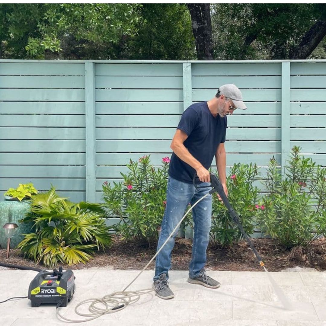A man using a pressure washer to clean an outdoor patio.