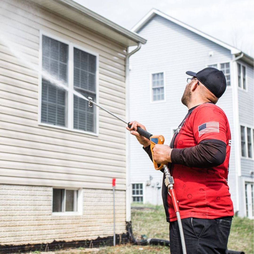 A man in a red shirt using a pressure washer to clean the exterior of a house.