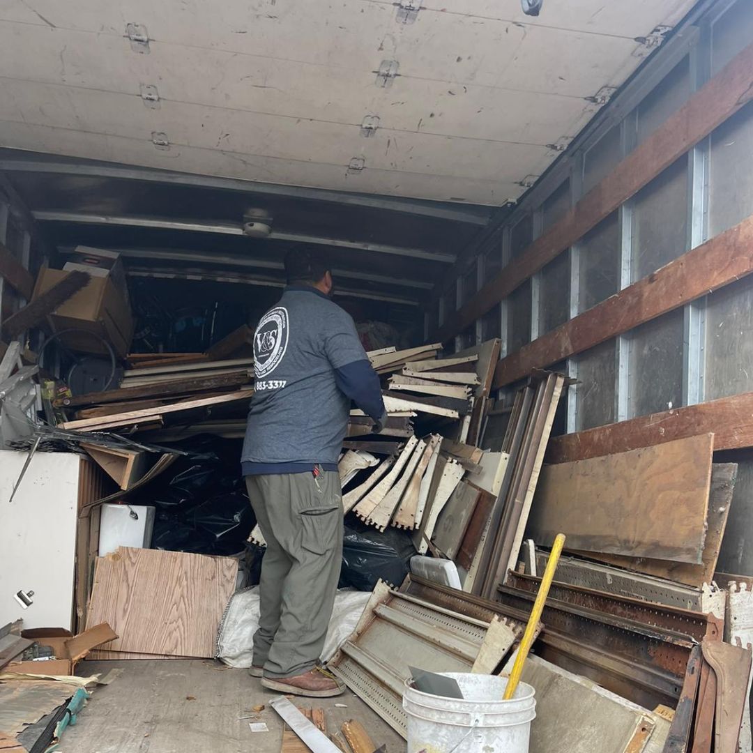 A man organizing and disposing of various debris and materials inside a large truck, involved in a junk removal or cleanup project.